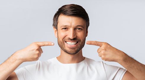 a man smiling and pointing at his teeth