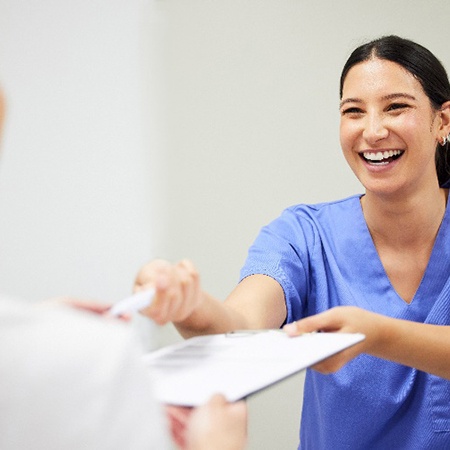 Smiling dental assistant handing patient forms