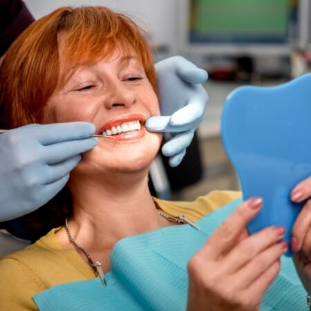 Woman with dental implants looking at smile in mirror