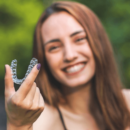 a woman in Novi smiling and holding Invisalign aligners 