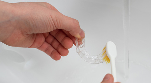 Patient cleaning clear aligner in sink