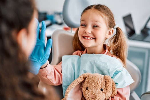Little girl with pigtails holding stuffed bunny high-fiving dentist