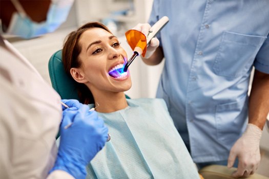 Dentist holding model implant with one hand and touching her cheek with the other