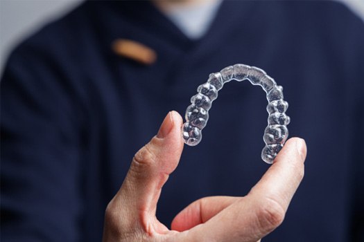 Woman in dental chair with eyes closed pressing hand to jaw to show dentist where it hurts