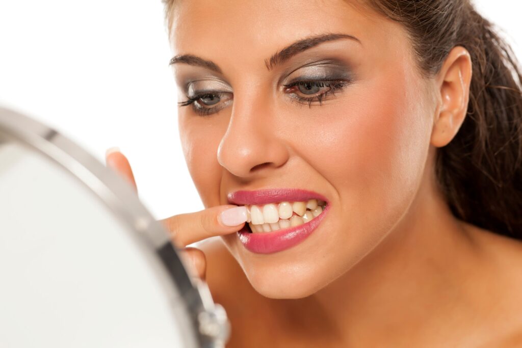 Woman with brown hair poking at teeth in front of a mirror